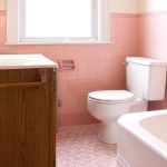Bathroom interior featuring a pink color scheme, including a toilet, bathtub, and wooden cabinet, relevant to plumbing services for older homes.